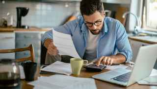 Man sitting at table with paperwork using calculator