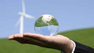 Hand holding a glass globe with windpower in the background