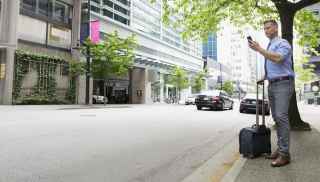 Man waiting on roadside curb with suitcase and phone