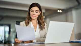 Business woman reading a document at her office desk with laptop