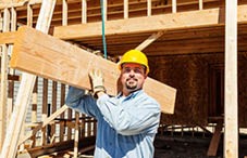 Construction worker with yellow hat carrying timber