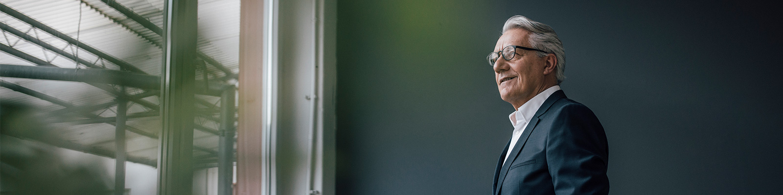 Older man standing against grey wall looking out window